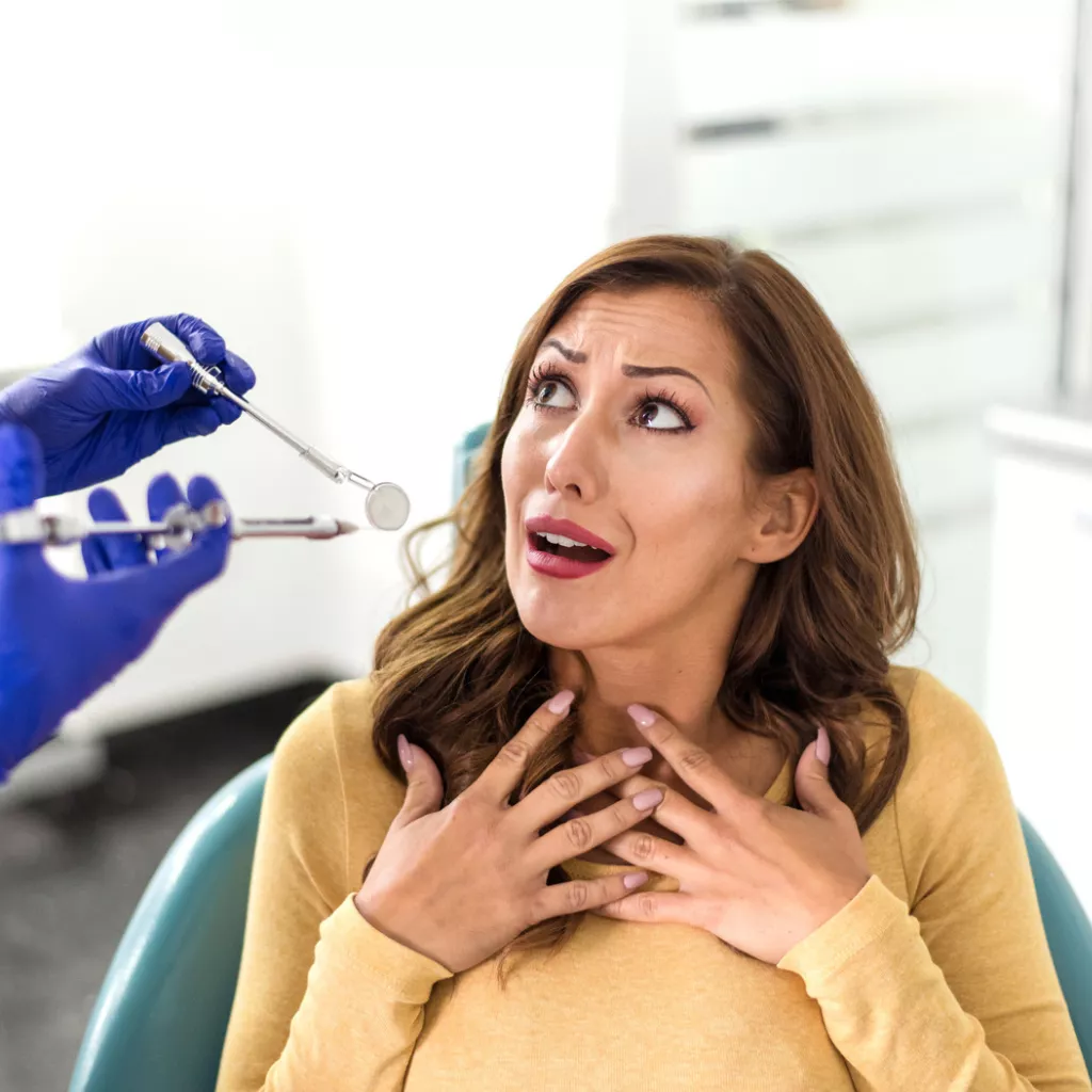 Nervous woman in a dental chair looking up at a dentist holding a mouth mirror and probe